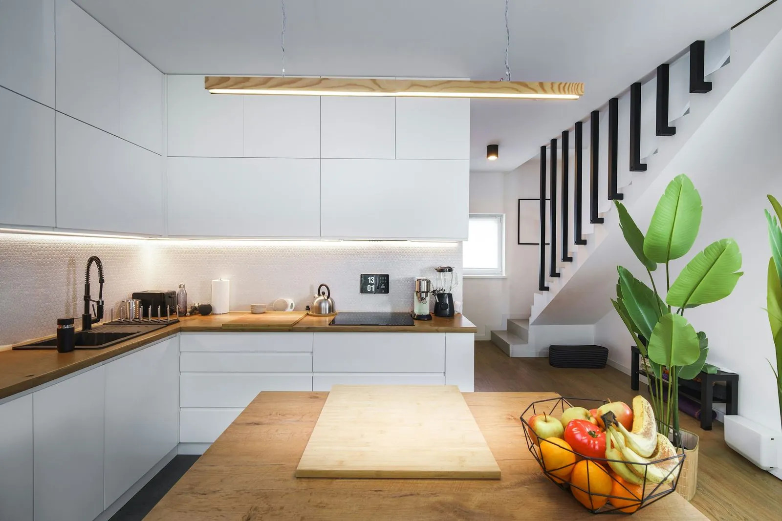Cocina blanca con isla de madera y escalera al fondo